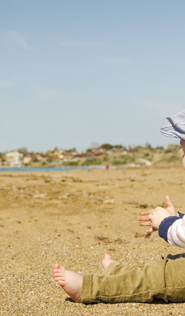 Маленький мальчик сидит на песке у реки