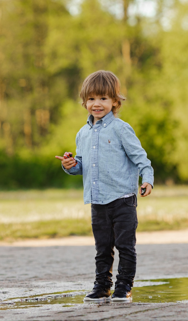 Маленький мальчик стоит в луже на дороге 