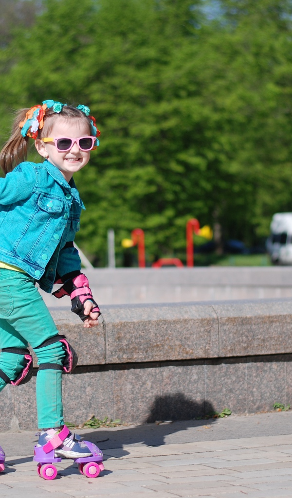 Маленькая веселая девочка катается на роликах