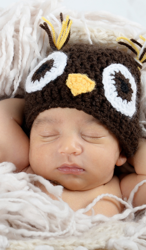 Маленький ребенок  в вязаной шапке спит на кровати 