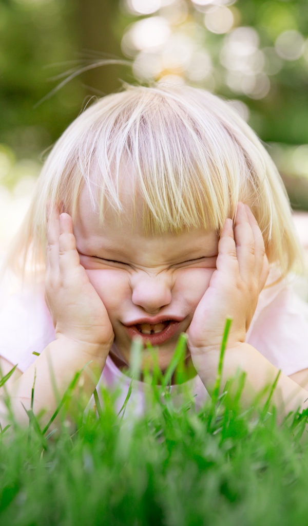 Маленькая смешная девочка лежит на зеленой траве 