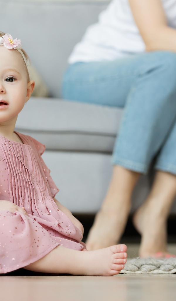 Маленькая девочка в розовом платье сидит на полу