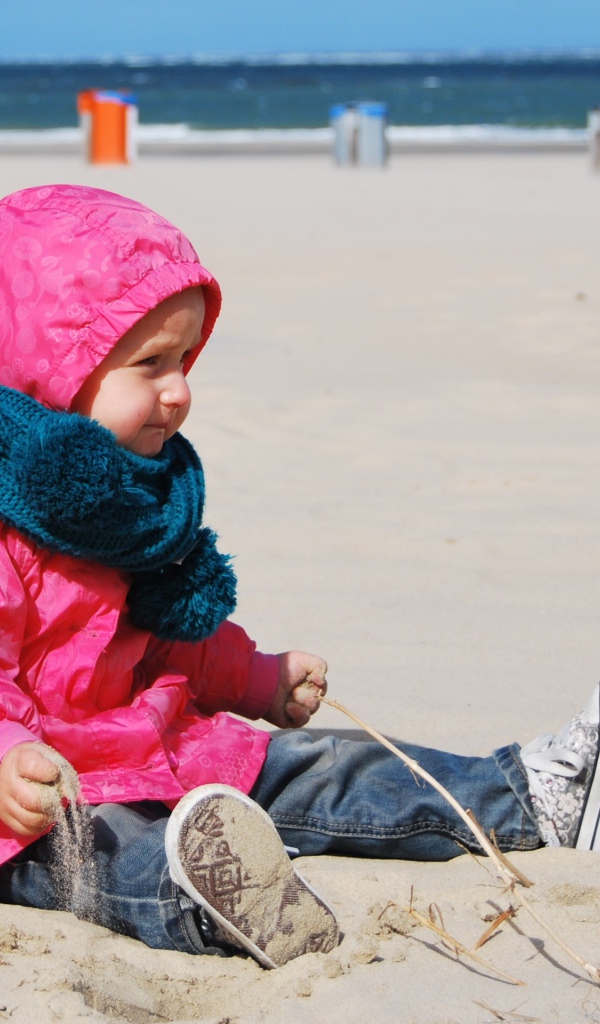 Маленькая девочка в розовой куртке на песке