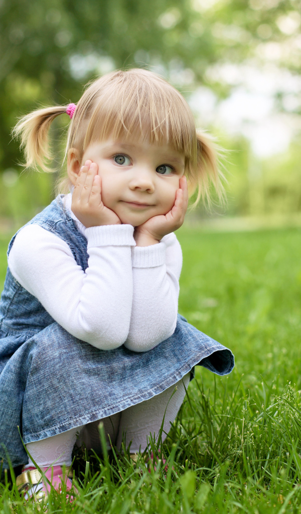 Маленькая девочка в сарафане сидит на траве 