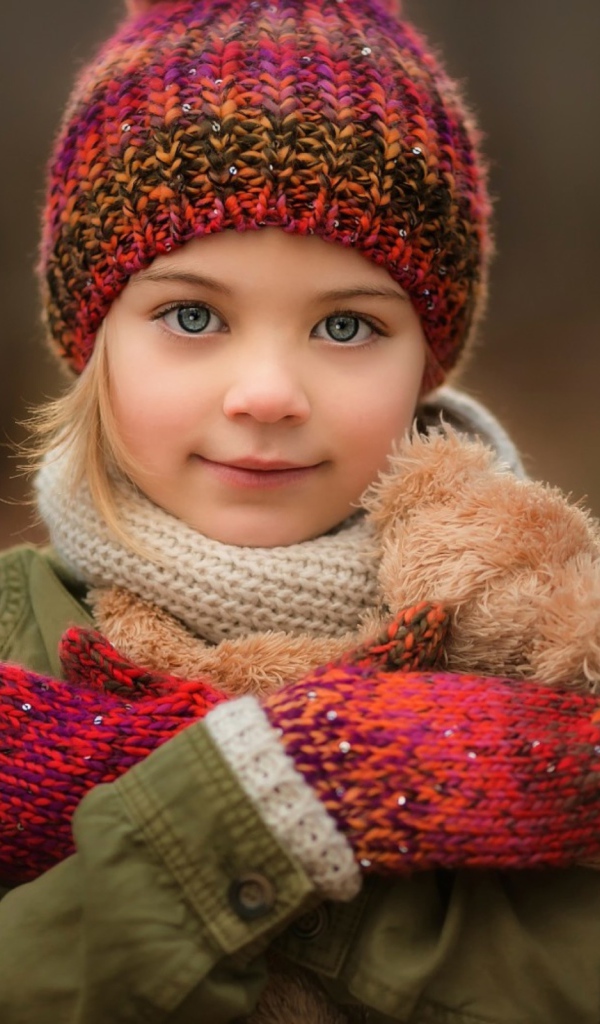 Маленькая девочка в теплой шапке и варежках  с игрушкой в руках 