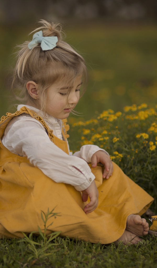 Маленькая девочка в желтом платье сидит на траве 