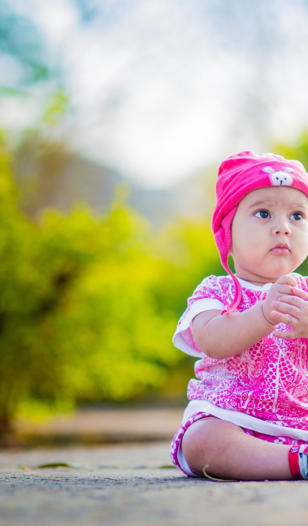 Маленькая девочка в розовом костюме сидит на земле