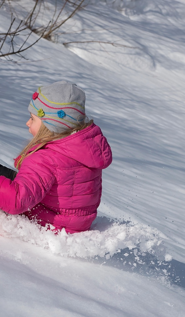 Маленькая девочка катится с заснеженной горки 