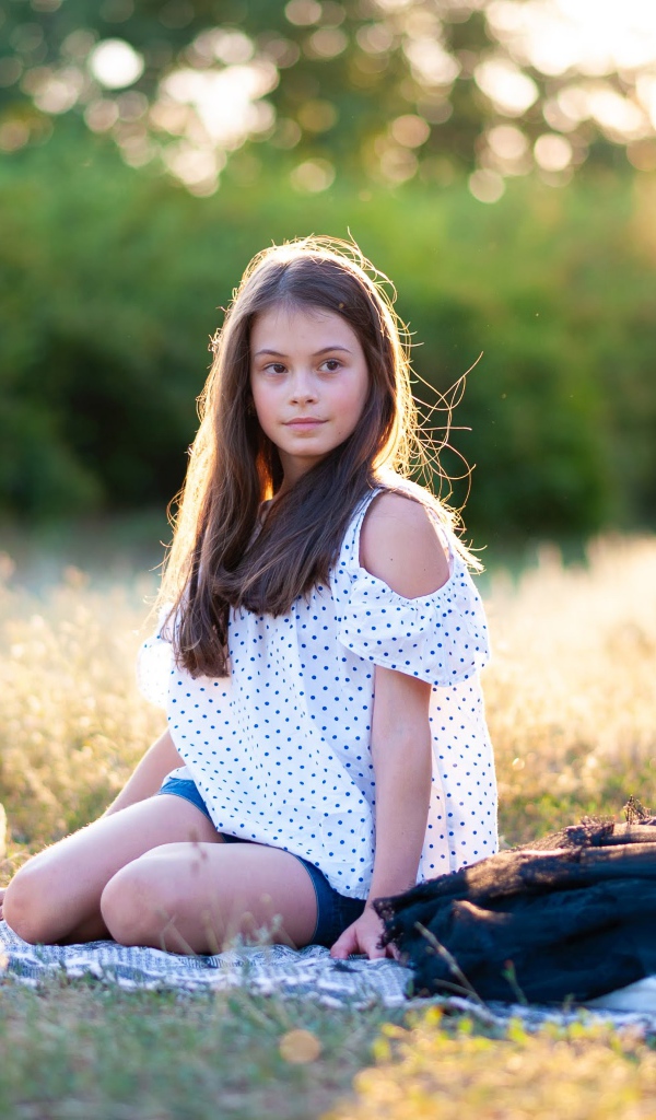 Маленькая девочка сидит на покрывале на земле 