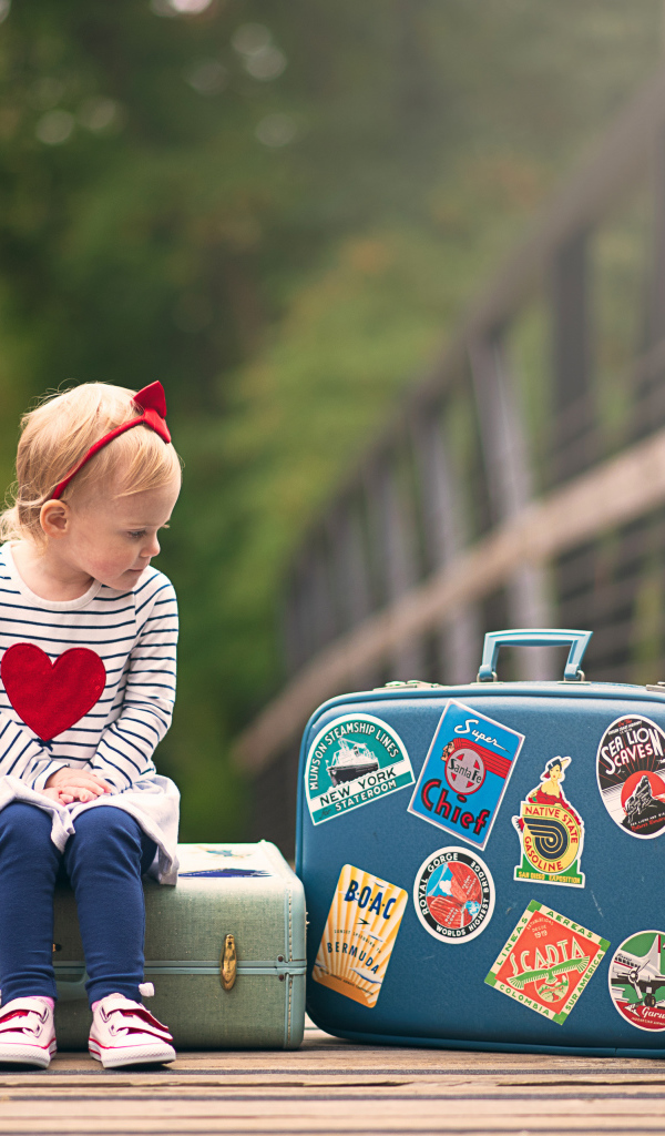 Маленькая девочка сидит на мосту с чемоданами