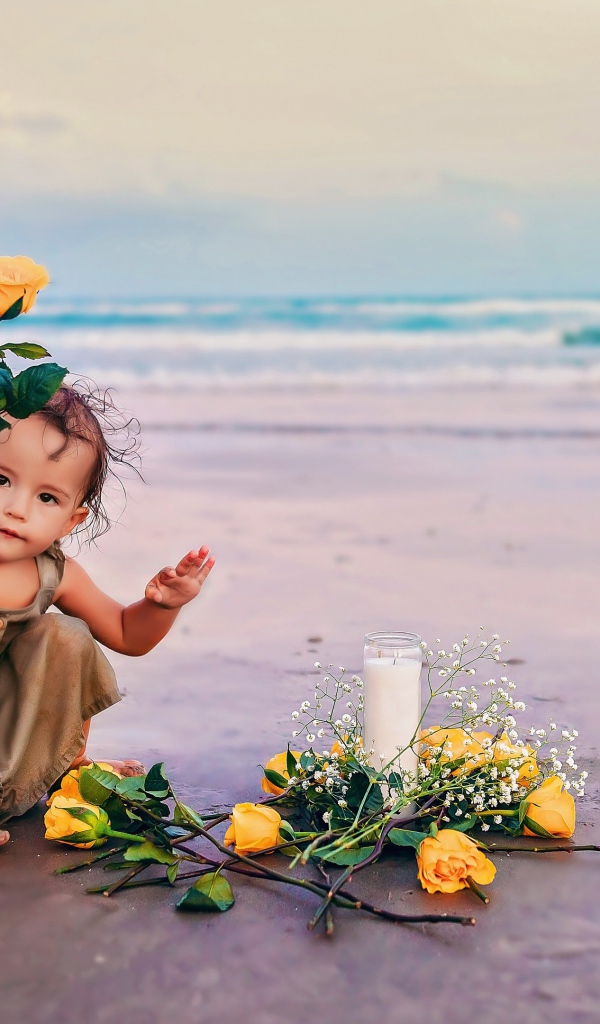 Маленькая девочка сидит на песке с розами 