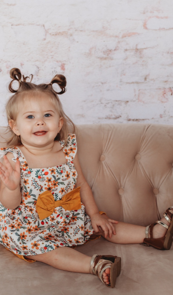 Маленькая девочка сидит на диване у стены