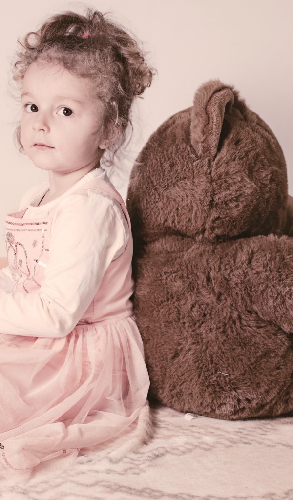 Маленькая девочка сидит с большим медведем