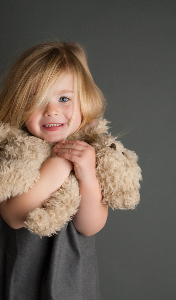 Маленькая девочка с игрушечным медвежонком в руках  на сером фоне 