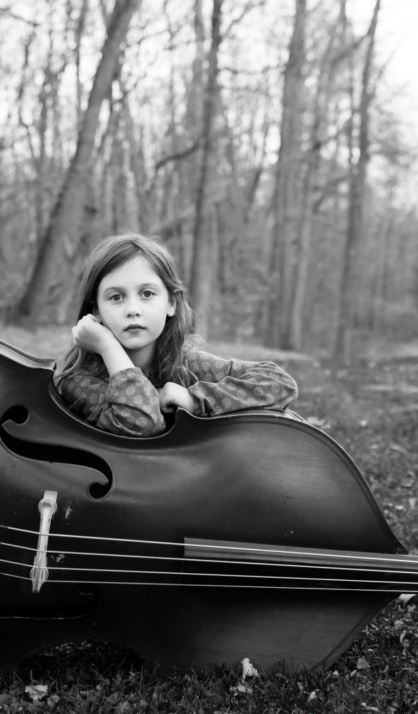 Маленькая девочка с виолончелью сидит в парке