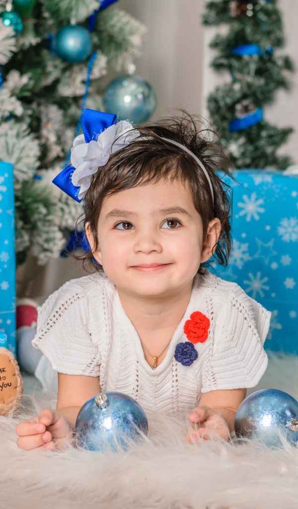 Маленькая девочка с подарками и игрушками под елкой 