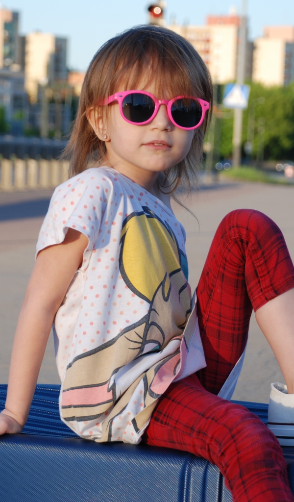 Маленькая девочка в очках сидит на чемодане