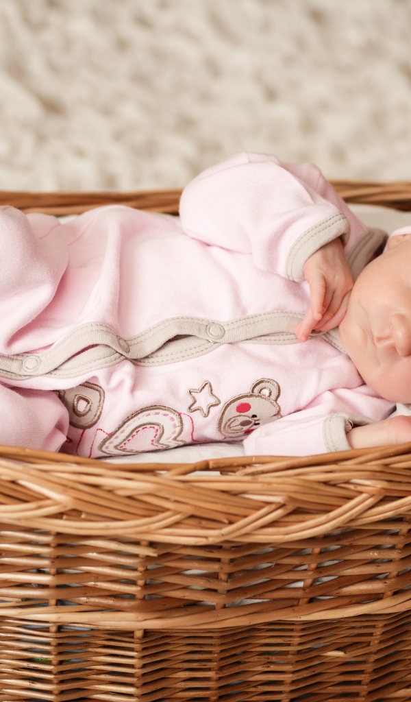 Маленькая новорожденная девочка в розовом костюме спит в корзине 