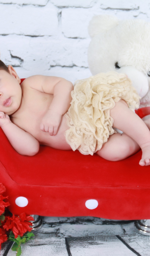 Маленькая принцесса лежит на красном диване у стены 