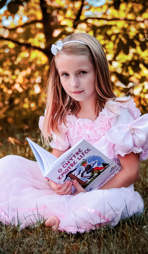 Маленькая принцесса сидит на траве с книгой