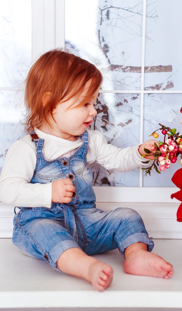 Маленькая рыжеволосая девочка сидит у корзины цветов 