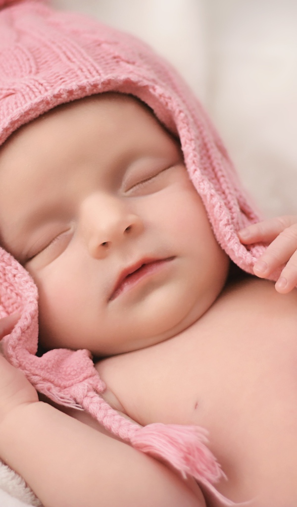 Маленький спящий ребенок в розовой вязаной шапке 