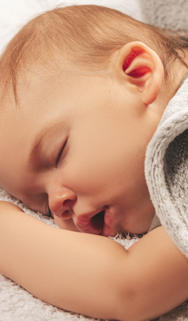 Маленький спящий ребенок под серым покрывалом 