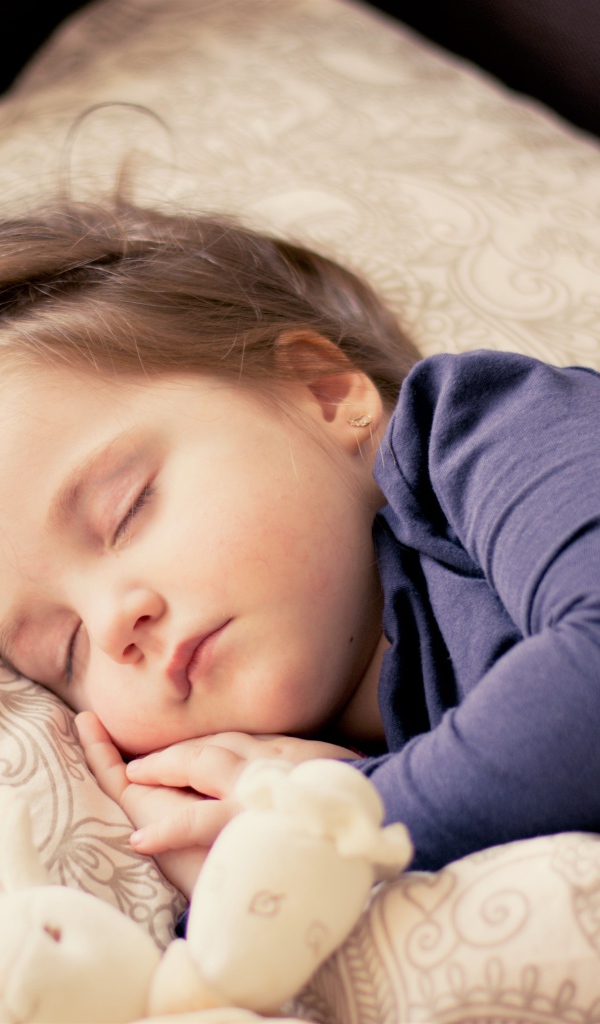 Маленькая спящая девочка на кровати с игрушкой 