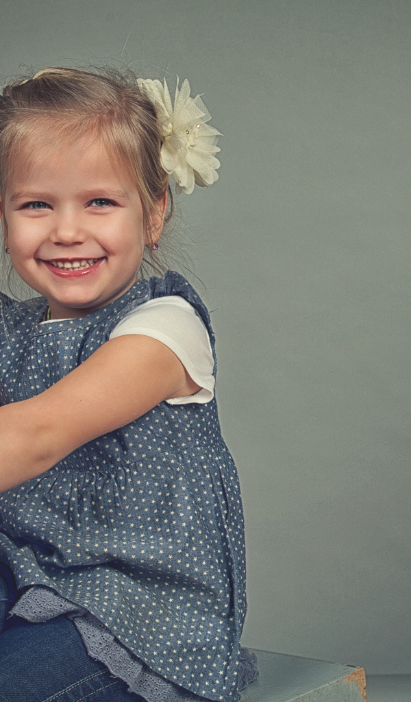 Маленькая улыбающаяся девочка с бантом на сером фоне 