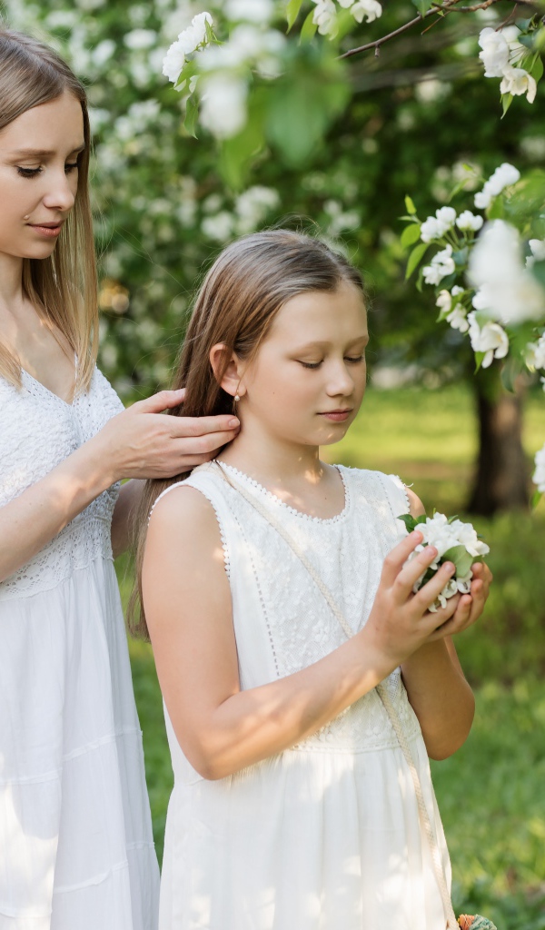 Мама заплетает дочке волосы у дерева