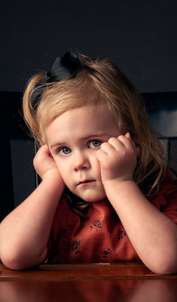 Грустная маленькая девочка сидит на черном стуле