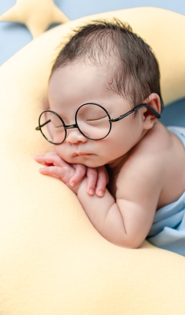 Спящий ребенок в очках на подушке в форме месяца