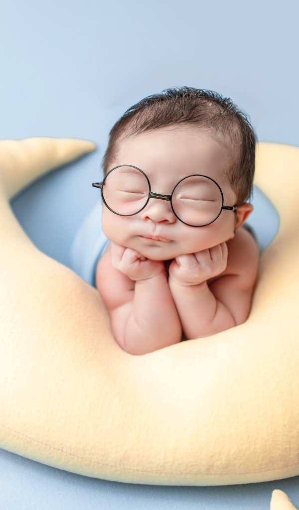 Спящий грудной ребенок в очках на желтой подушке 