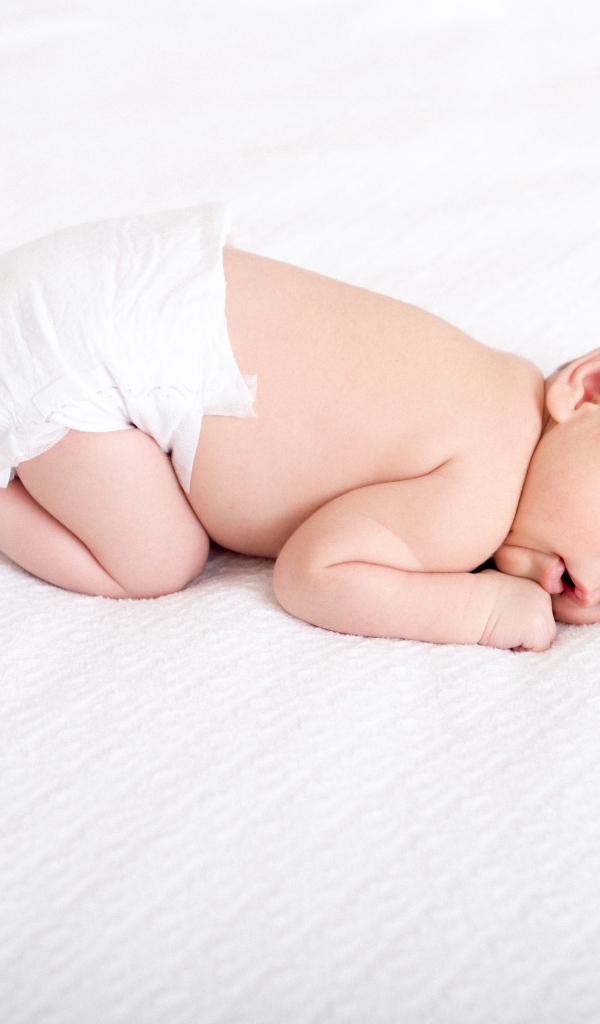 Маленький грудной ребенок в памперсе спит на белом фоне