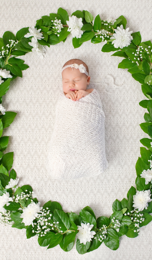 Маленький грудной ребенок спит в зеленом венке из листьев 