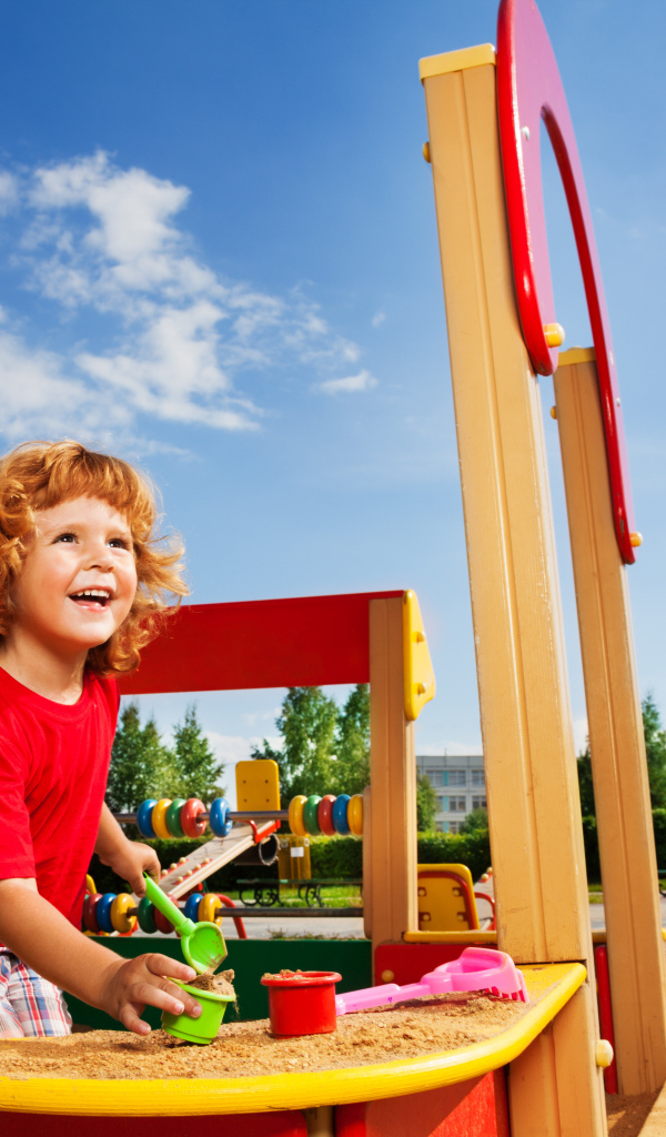 Улыбающийся мальчик в песочнице на детской площадке 