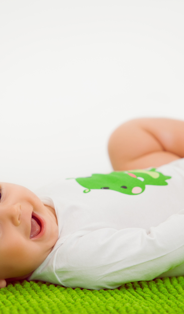 Улыбающийся маленький ребенок лежит на зеленом покрывале 