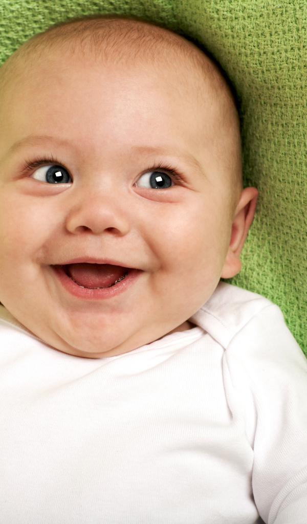 Улыбающийся маленький ребенок на зеленом покрывале 