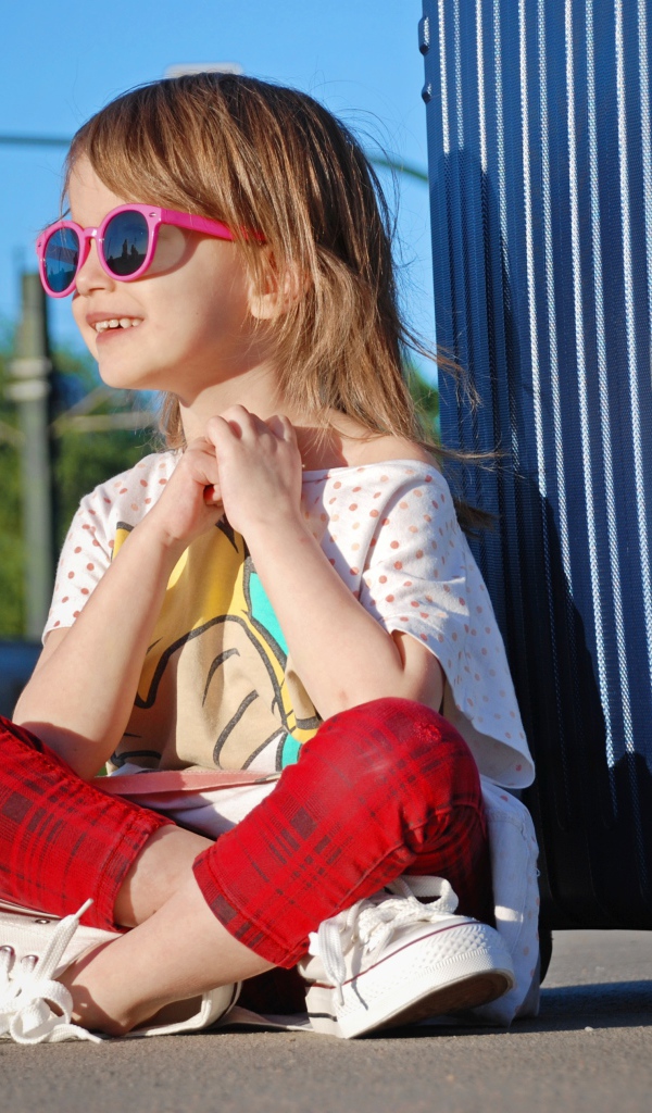 Улыбающаяся маленькая девочка в очках с чемоданом