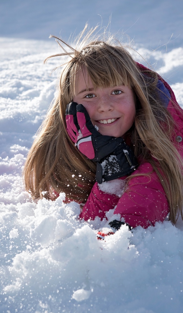 Улыбающаяся маленькая девочка лежит на снегу