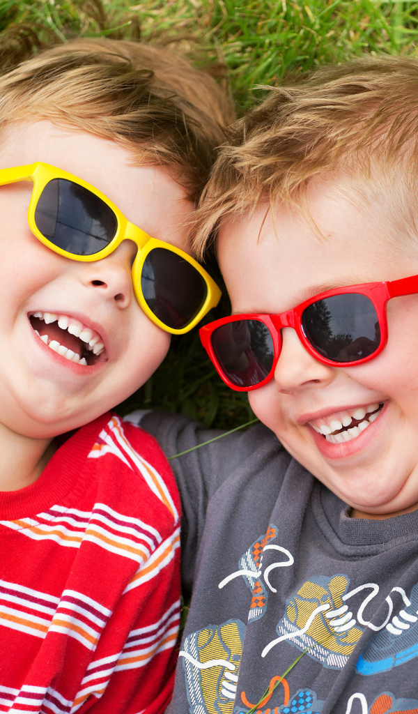 Два улыбающихся мальчика в очках на зеленой траве 