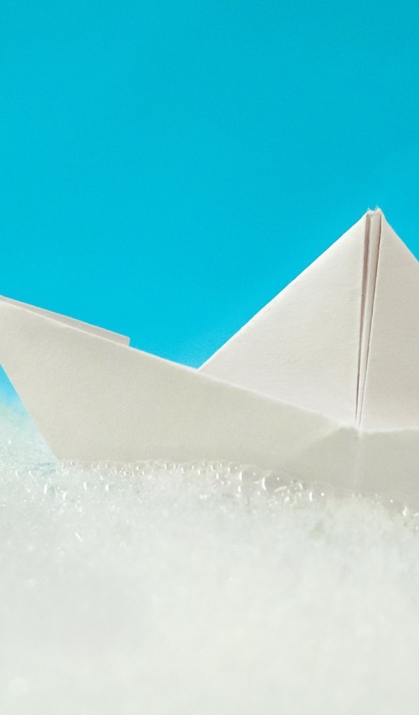 Белый бумажный кораблик на пене на голубом фоне