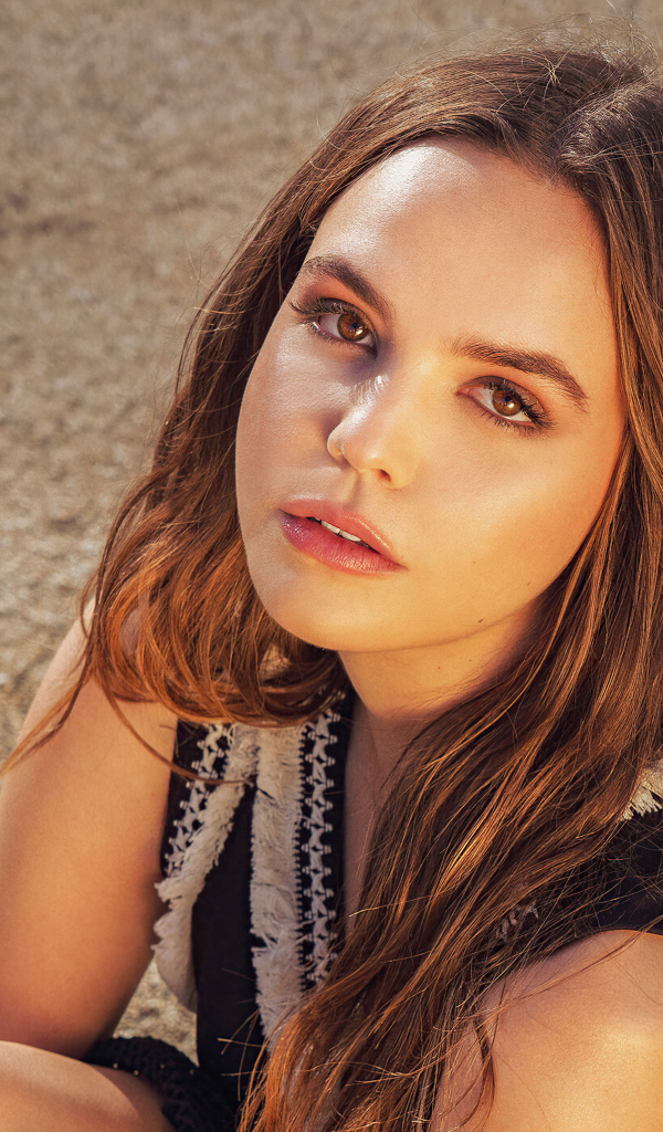 Кареглазая актриса Бэйли Мэдисон сидит на песке