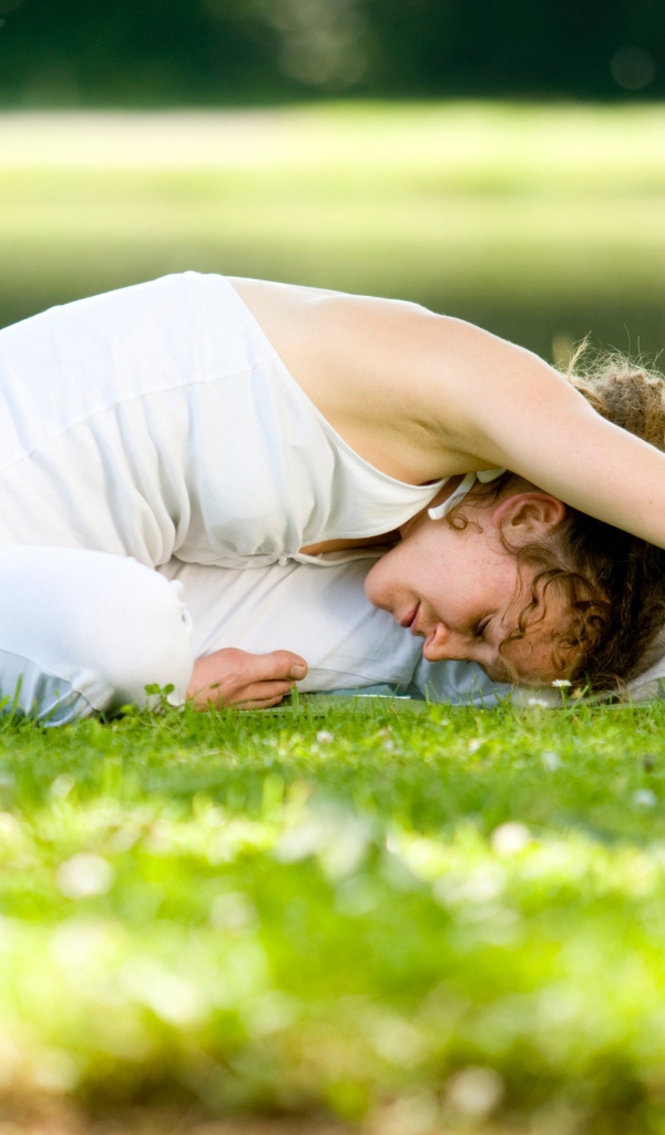 Девушка в белом костюме занимается йогой на траве
