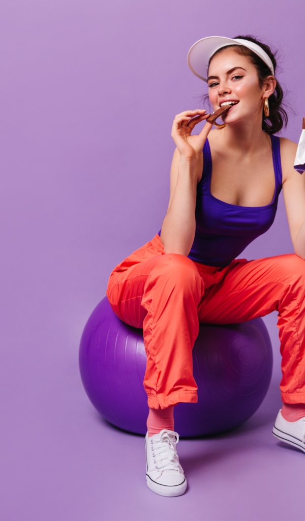 Девушка с шоколадкой сидит на фитболе
