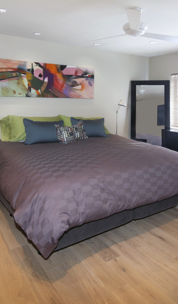 Большая серая кровать в спальне с белыми стенами