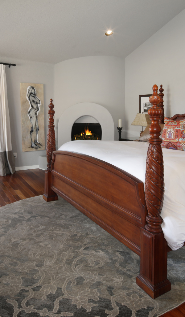 Большая деревянная кровать в спальне с камином 