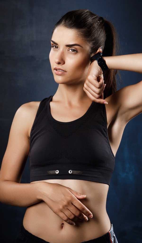 Спортивная девушка в черном топике с часами на руке 