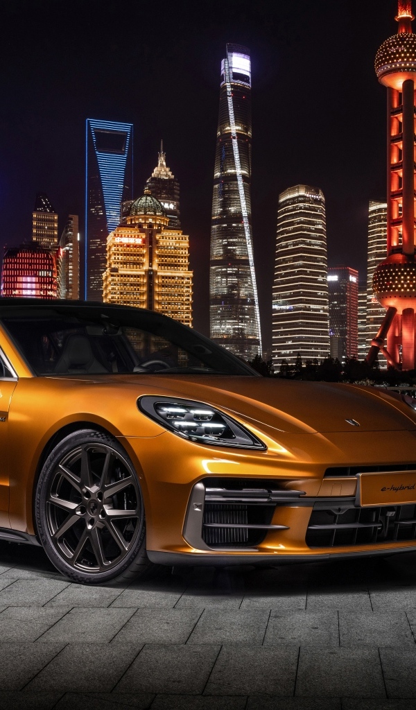 Золотистый автомобиль Porsche Panamera Turbo E-Hybrid 2024 года на фоне города