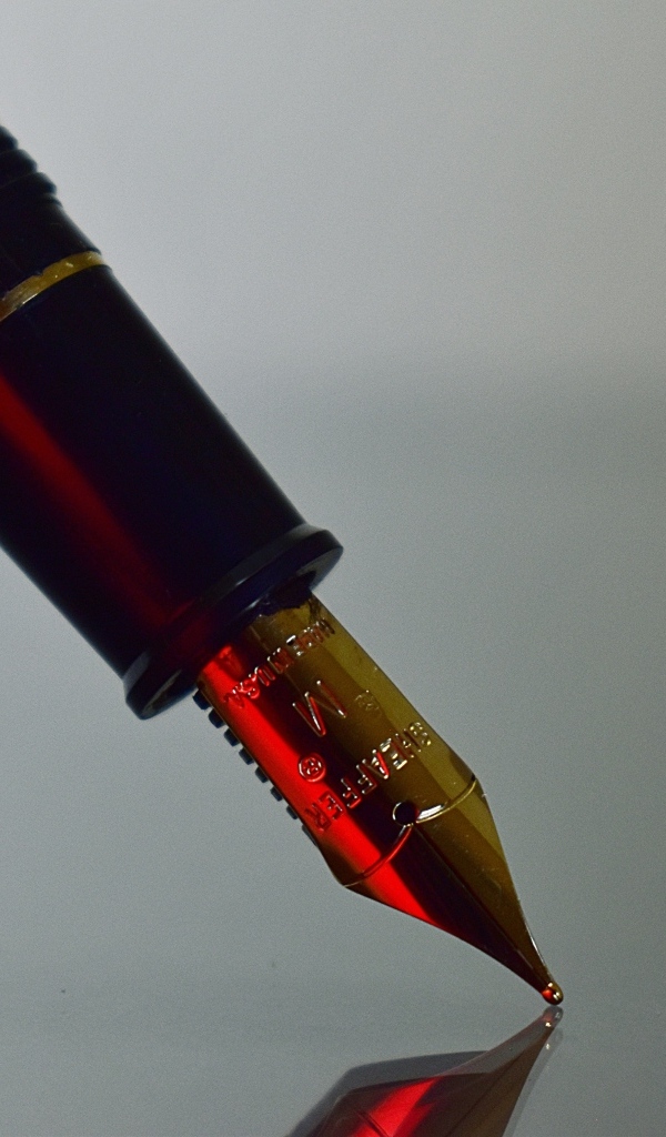 Золотое перо чернильной ручки на сером фоне